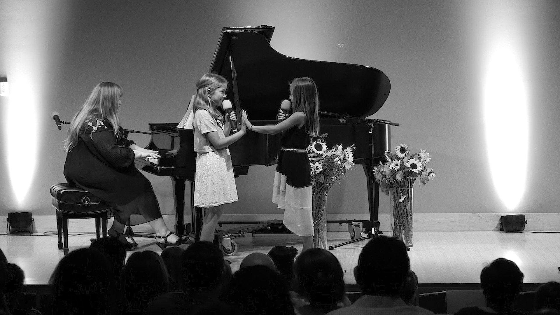 Two students singing together on a small stage